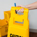 A person holding a yellow Rubbermaid "Caution Wet Floor" sign.