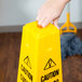 A hand holding a yellow Rubbermaid caution wet floor sign.