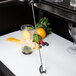 A Barfly stainless steel bar spoon with muddler stirring a glass of fruit juice.