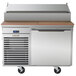 A stainless steel Traulsen commercial pizza prep table on wheels with a wooden top.
