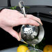 A person holding a Barfly stainless steel julep strainer and pouring liquid into it.
