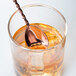 A copper Barfly bar spoon in a glass of liquid.