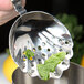 A hand holding a Barfly stainless steel scalloped julep strainer with mint leaves.
