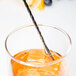 A Barfly stainless steel bar spoon in a glass of orange juice with a straw.