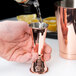 A person using a Barfly copper-plated Japanese style jigger to pour liquid into a cup.