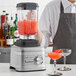 A man in an apron using a KitchenAid Contour Silver commercial blender to make a drink.
