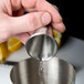 A hand pouring liquid into a Barfly stainless steel jigger.