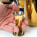 A person using a Barfly gold-plated Japanese style jigger to pour liquid into a gold cup.