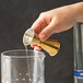 A hand using a Barfly gold-plated Japanese style jigger to pour liquid into a glass.