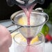 A person using a Barfly stainless steel conical fine mesh strainer to pour a purple drink with ice and fruit.