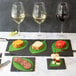 A table with a rectangular black slate tray with a piece of food on it and a glass of white wine.