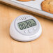 A Taylor digital kitchen timer with clock on a table with cookies.