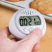 A person's hand holding a Taylor digital kitchen timer showing the time.