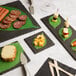 A group of Acopa black slate plates with a variety of food items on them.