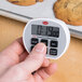 A hand using a Cooper-Atkins digital kitchen timer to count down while baking cookies.