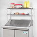 An Avantco stainless steel double deck overshelf on a counter with two shelves.
