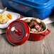 A red GET enamel oval pot with a lid filled with food next to a plate of rice and a blue container.