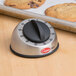 A Cooper-Atkins stainless steel mechanical kitchen timer with a black dial on a baking tray with cookies.