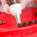 A person using an Ateco closed star piping tip to decorate a cake with chocolate icing.