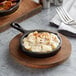 A Valor pre-seasoned mini cast iron skillet filled with food with white sauce on a wooden surface.