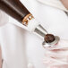 A person using an Ateco curved petal piping tip to inject a liquid into a chocolate dessert.