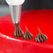 A pastry chef using an Ateco closed star piping tip to make brown frosting on a cake.