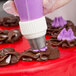 A person using an Ateco pastry bag with a Russian piping tip to decorate a cake with purple icing.