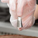 A gloved hand holding an Ateco curved petal piping tip nozzle over a pastry bag.