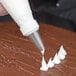 A person using an Ateco plain piping tip on a pastry bag to pipe white frosting.