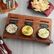 A wooden board with bowls of dips and a Valor mini cast iron skillet of cheese dip with jalapenos and a bowl of chips.