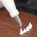 A person using an Ateco plain piping tip to pipe white frosting.
