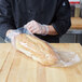 A person in a chef's uniform holding a plastic bag of bread.
