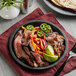 A Valor pre-seasoned cast iron fajita skillet with steak, peppers, and onions on a table.