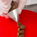 A person using an Ateco rose piping tip to pipe chocolate frosting on a cake.