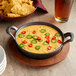 A Valor pre-seasoned cast iron round casserole dish filled with food on a table with a bowl of chips and a glass of beer.