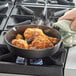 A person cooking fried chicken in a Valor cast iron skillet on a stove.