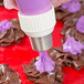 A person's hand using an Ateco Russian piping tip to pipe purple frosting on a chocolate flower.