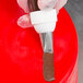 A hand using an Ateco rose leaf piping tip to pipe brown icing on a red surface.