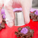 A person in gloves using an Ateco Russian piping tip to pipe chocolate flowers on a red plate.
