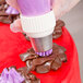 A plastic gloved hand using a white and purple Ateco pastry bag tip to decorate chocolate.