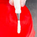 A person using an Ateco leaf piping tip with a white pastry bag over a red surface.