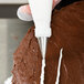 A person using an Ateco cross-top piping tip on a pastry bag to frost a chocolate cake.