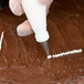 A hand using an Ateco Cross-Top piping tip to decorate a cake with a pastry bag.