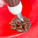 A hand using an Ateco Russian ball tip piping tip to pipe chocolate frosting onto a red cake.