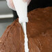 A person's hand using an Ateco leaf piping tip in a pastry bag to frost a chocolate cake.