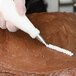 A person's hand using an Ateco leaf piping tip in a pastry bag to frost a cake.