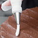 A person using an Ateco closed star piping tip to frost a chocolate cake.