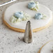 A close up of a metal Ateco leaf piping tip next to a cookie with white icing.