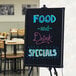 A black Choice illuminated LED write-on sign with food and drink specials written on it.
