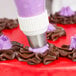 A person using an Ateco pastry bag to pipe purple frosting on a cake.